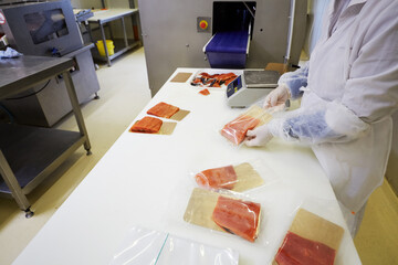Worker puts pieces of red saltfish on foiled paper into packages at fish factory