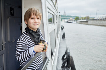 Boy in striped vest with binoculars stands at railings on pleasure boat deck