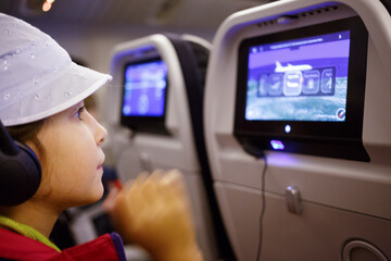 Girl with headphones watching the monitor in the aircraft seat