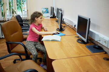 Little girl sits alone at table with computer monitor at computer room
