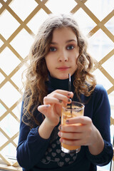 Pretty girl holds cocktail near wooden fence indoor and looks at camera