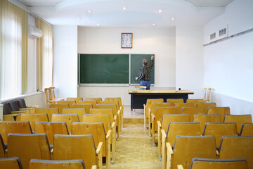 Teacher clears with blackboard in empty classroom, back view
