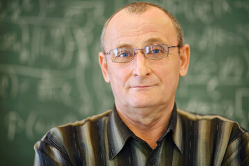 Old teacher in glasses near blackboard in school classroom, shallow dof