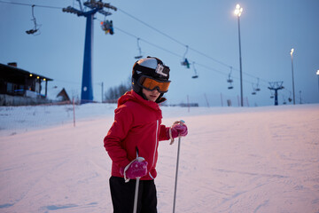 Girl in helmet with camera skiing on snowy slope at ski resort in evening