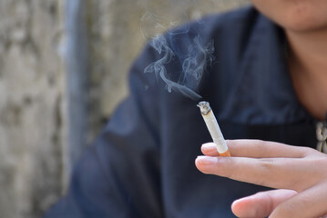 Closeup hand holding lighted cigarrette in private area of asian teenager boy, white smoke edited,...