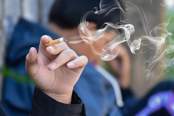 Closeup hand holding lighted cigarrette in private area of asian teenager boy, white smoke edited, concept for teenager's problem with drugs around the world, new edited. - obrazy, fototapety, plakaty
