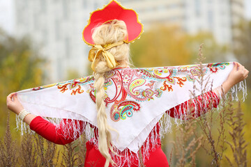 Pretty woman in traditional russian kokoshnik with kerchief, long braid poses outdoor, back view
