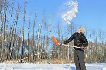 Boy in clearing in winter woods vigorously tosses snow shovel