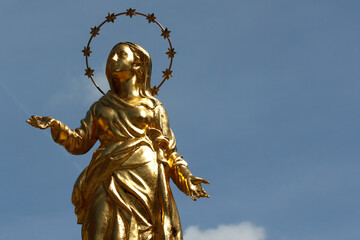 Golden Virgin Mary statue against blue sky. - obrazy, fototapety, plakaty