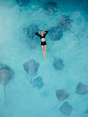 Woman swimming with stingrays in Maldives. Sting ray fishes and woman swimming in blue sea, Aerial...