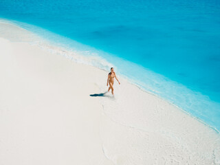 Woman in swimsuit walking on tropical white sandy beach with turquoise ocean water. Aerial view © artifirsov