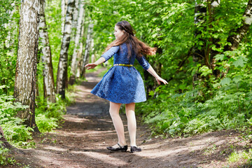 Little girl in dark-blue dress spins in dance on pathway in summer park - obrazy, fototapety, plakaty