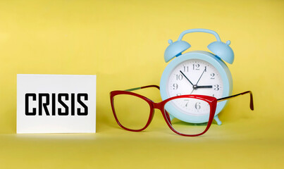 Notepad with crisis sign, business financial loss, crisis concept on yellow background with alarm clock and glasses