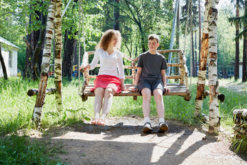 Mother and son sit on wooden swings made of birch in the park
