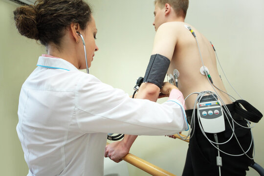 Nurse putting on cuff of device for measuring patients blood pressure during exercise ECG in hospital