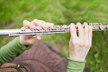 Female hands hold metal flute against green grass
