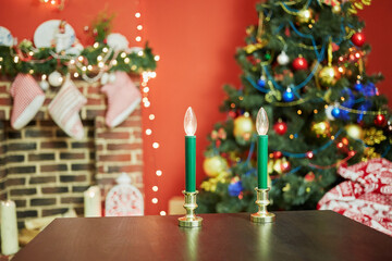 Interior of room with firtree decorated to christmas holidays, fireplace, red walls. Focus  on electric candles at table.