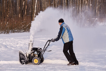 Man removes snow with gas snow thrower at winter day