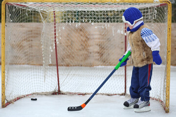Little boy on skates with a hockey stick stands at the gate