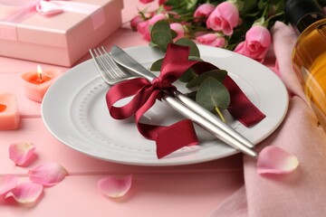 Place setting with roses and candles on pink table, closeup. Romantic dinner