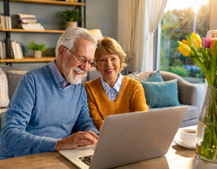 Senior couple using laptop computer at home having video call with grandchildren