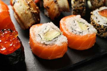 Set of delicious sushi rolls on black table, closeup