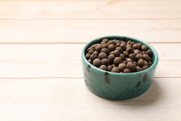 Dry allspice berries (Jamaica pepper) in bowl on light wooden table, space for text