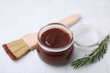 Marinade in jar, rosemary and basting brush on white tiled table