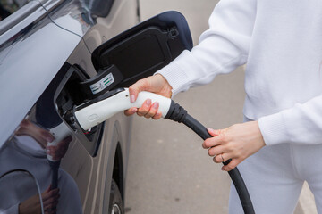 Young woman charging her electric car at a charging station in the city. Eco fuel concept. The...