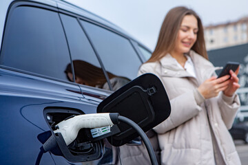 Young woman charging her electric car at a charging station in the city. Eco fuel concept. The...