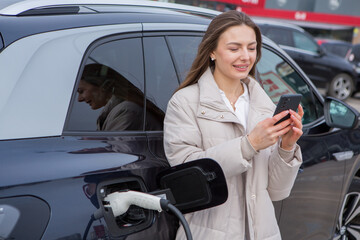 Young woman charging her electric car at a charging station in the city. Eco fuel concept. The...