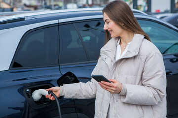 Young woman charging her electric car at a charging station in the city. Eco fuel concept. The...