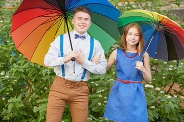 Teenage boy and girl stand with rainbow coloured umbrellas outdoor - Powered by Adobe