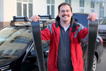 Happy man in a red jacket with downhill skiing standing about the car in the parking