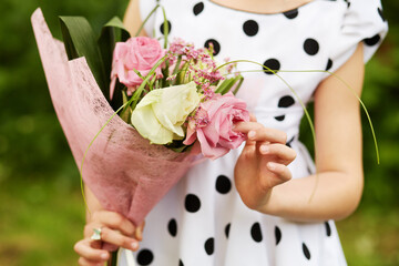Body and hands of girl who holds bunch of flowers outdoor.