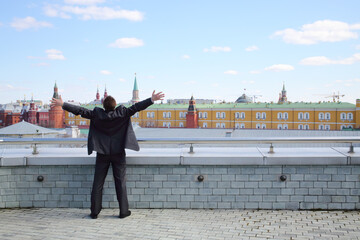 Man in a business suit with his arms raised standing on the terrace overlooking the Kremlin, view...