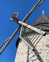 Fieldstone windmill with wooden roof. Mill blades grinding under a blue sky. Brick tower with rotor...