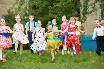 Group of eleven children dressed in dance suits runs across grassy lawn