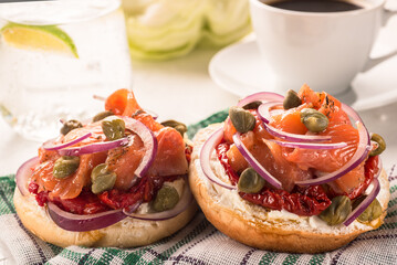 Two sandwiches with cheese cream, red fish, onions and capers on a napkin against the background of a cup of black coffee close-up.