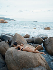 Fototapeta na wymiar Summer Sensation: A Stunning Brunette in Sexy Swimwear Poses on a Rock by the Ocean