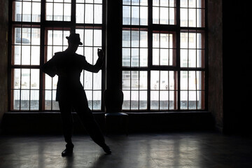 Silhouette of man in black suit and hat dancing tango in room with big window