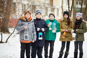 Five children stand together, holding home-made bird feeders with seeds and crumbs
