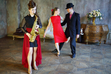 Couple dancing tango near girl playing saxophone. Pair out of focus