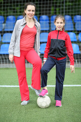 Portrait of a mother and daughter in tracksuits and the ball at the stadium