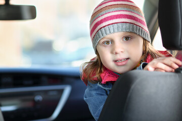 Portrait of little girl in pink waistcoat and striped hat sitting in car
