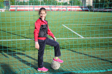 Portrait of a happy girl in tracksuits with the ball against the grid at the stadium