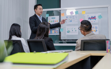 A man is giving a presentation to a group of people in a conference room. The presentation is about graphs and charts