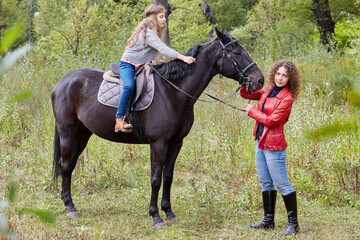 Woman in red jacket holds by the bridle horse on whom her daughter sits.