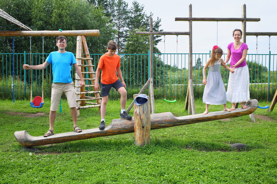 Parents with son and daughter teetering on a swing on a wooden playground