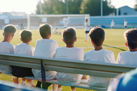 Boys in a football team sitting on the bench. Kids as soccer substitute players watching the game and waiting for a chance to play the match